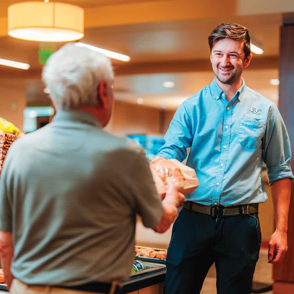 A man hands a package to a senior citizen