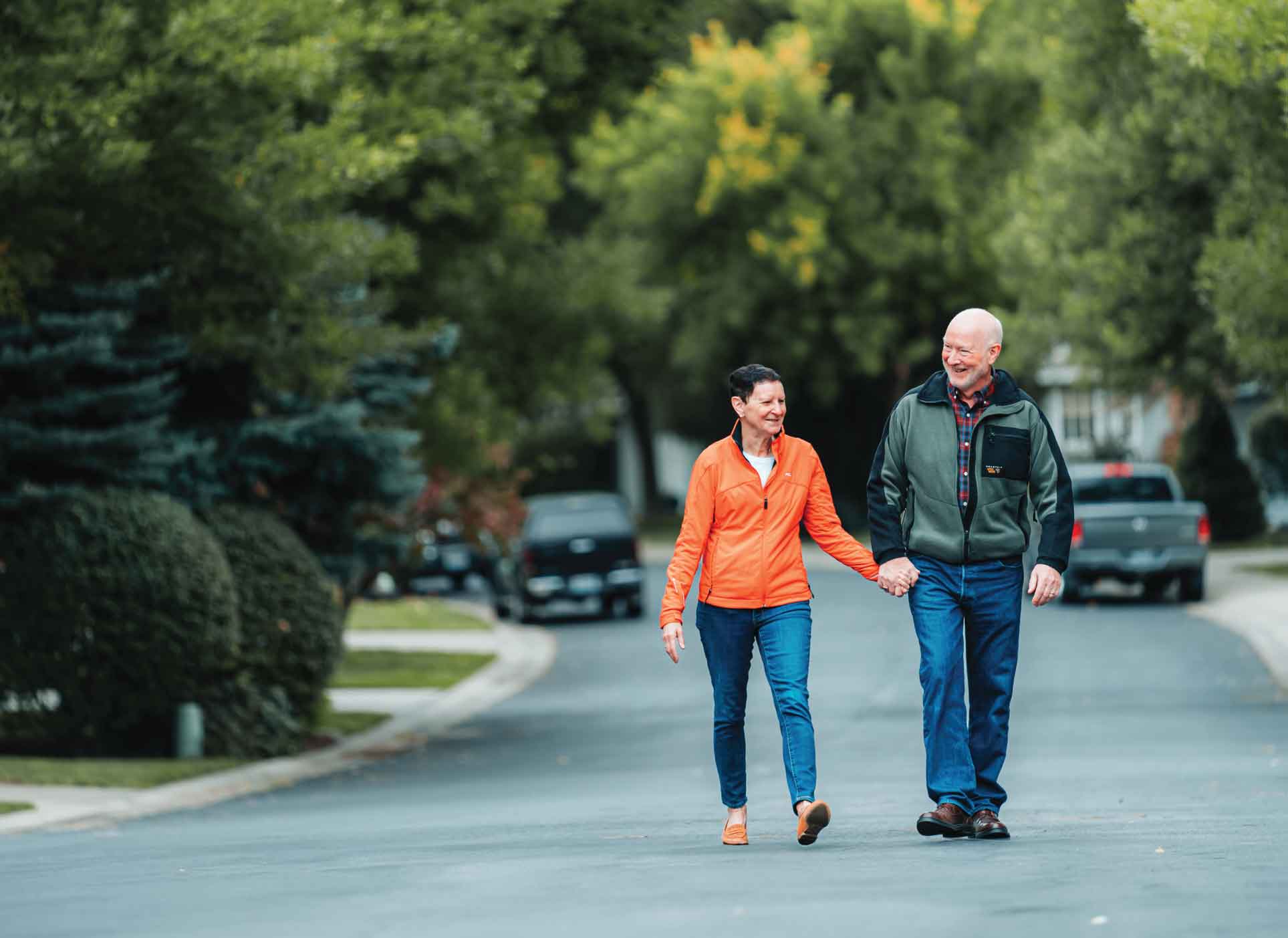 A senior couple walk down a paved road in a wooded area